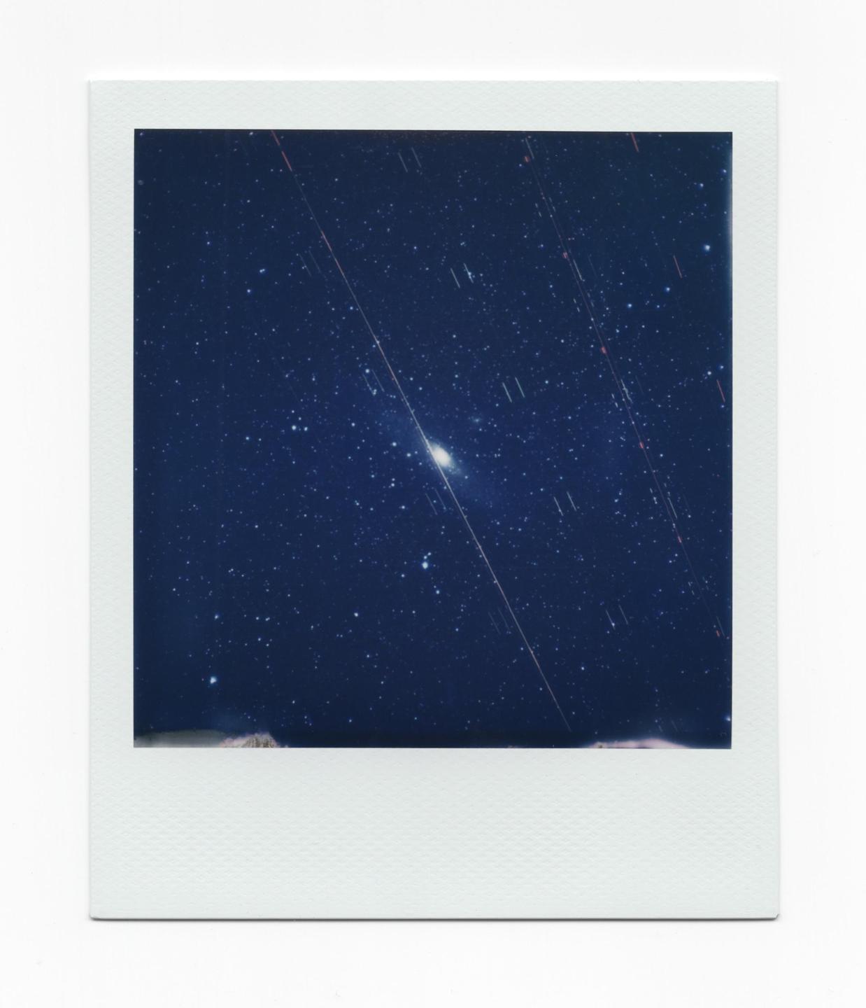 The Andromeda galaxy is visible in the night sky with many stars and light trails.