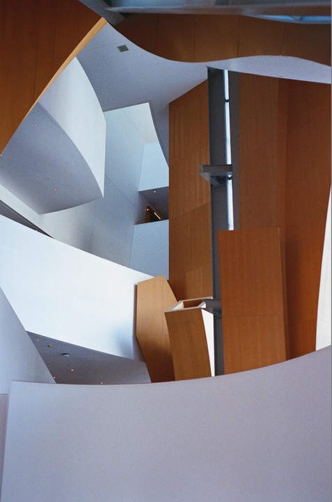 The interior of a building features curved and angular walls in white and wood tones.