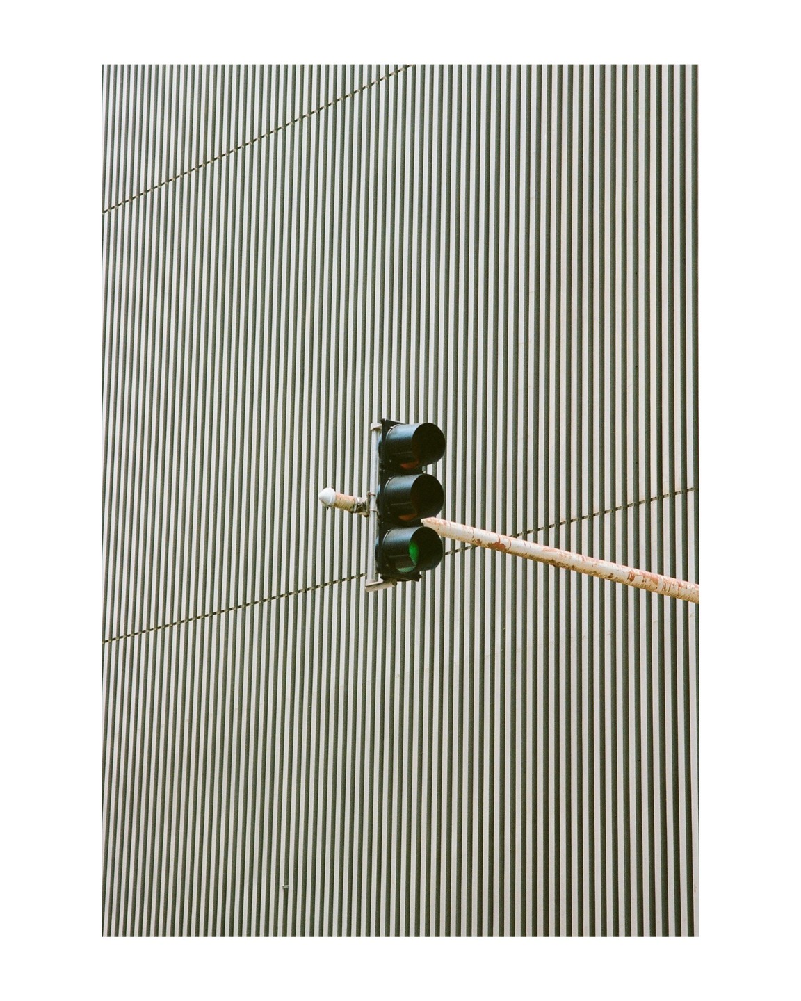 A traffic light with a green signal is mounted on a pole in front of a building with vertical stripes.