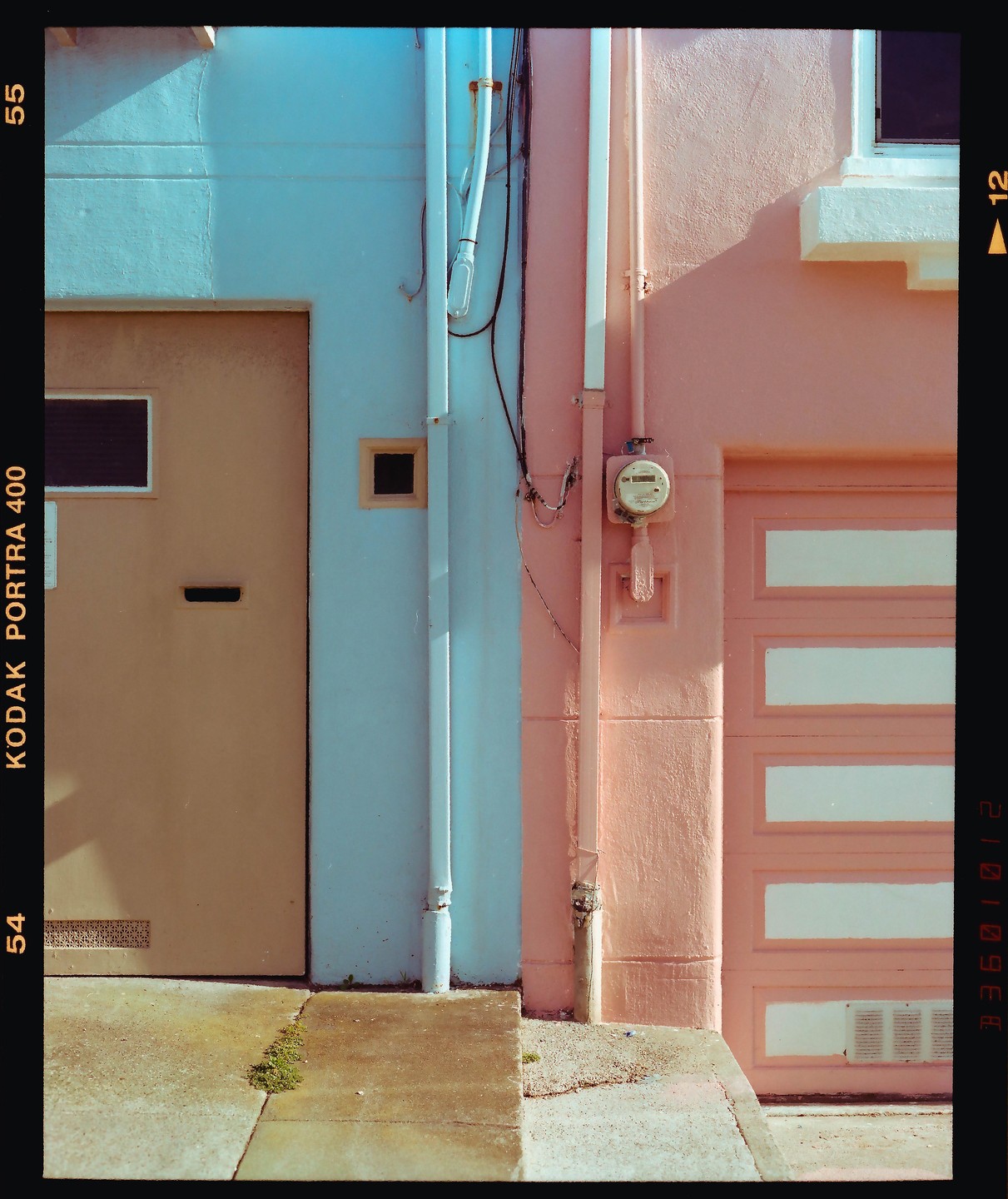 A light blue building with a brown door stands next to a pink building with a garage door.