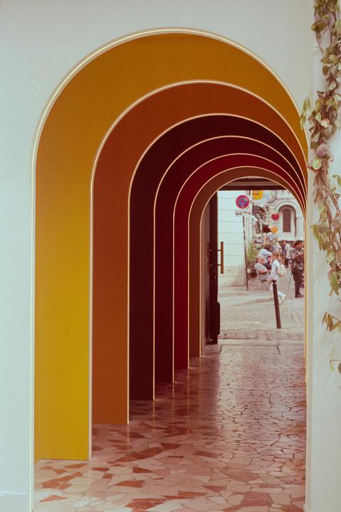 A series of colorful arches leads to a street with people and buildings.