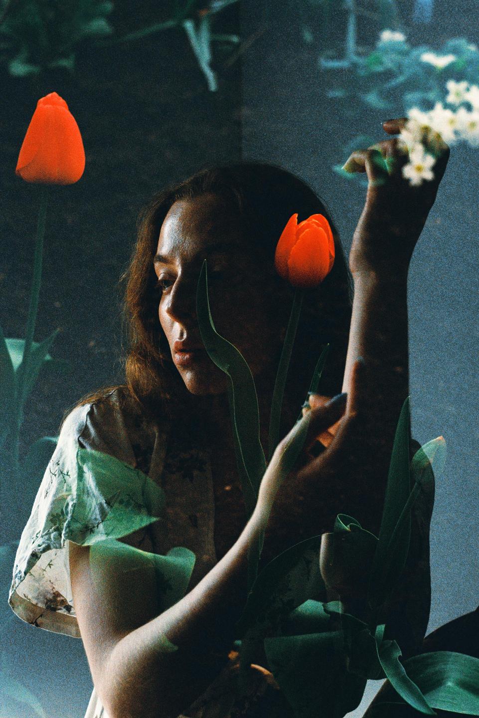 A woman with long hair is surrounded by red tulips and other foliage in a double exposure.