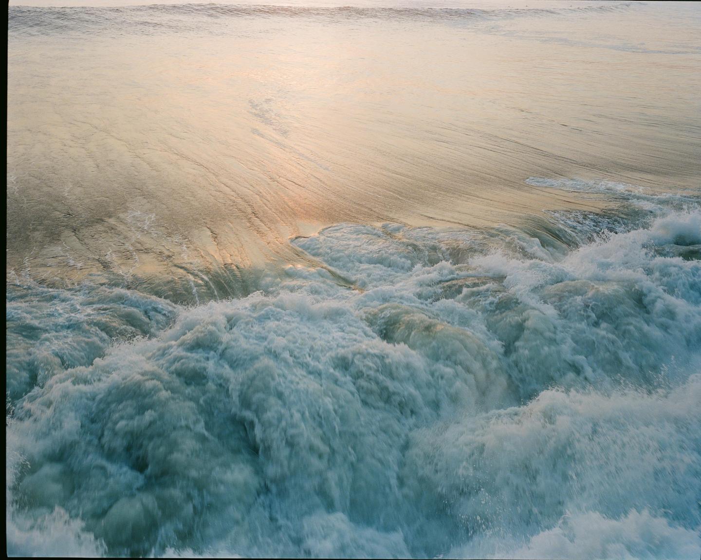 Ocean waves crash and foam, with the water reflecting a warm, golden light.