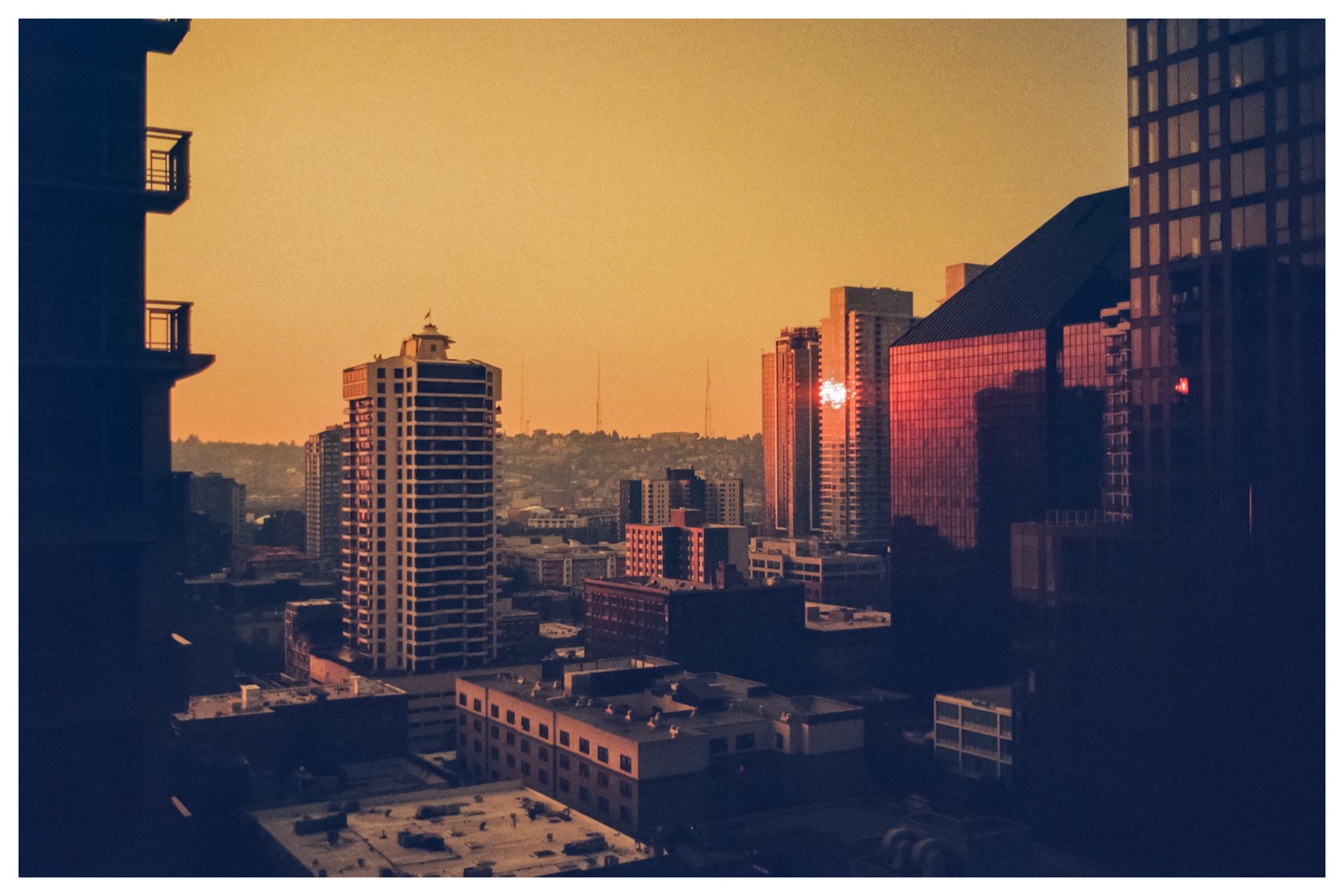 A city skyline with tall buildings is visible under a golden sky at sunset.