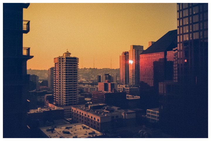 A city skyline with tall buildings is visible under a golden sky at sunset.