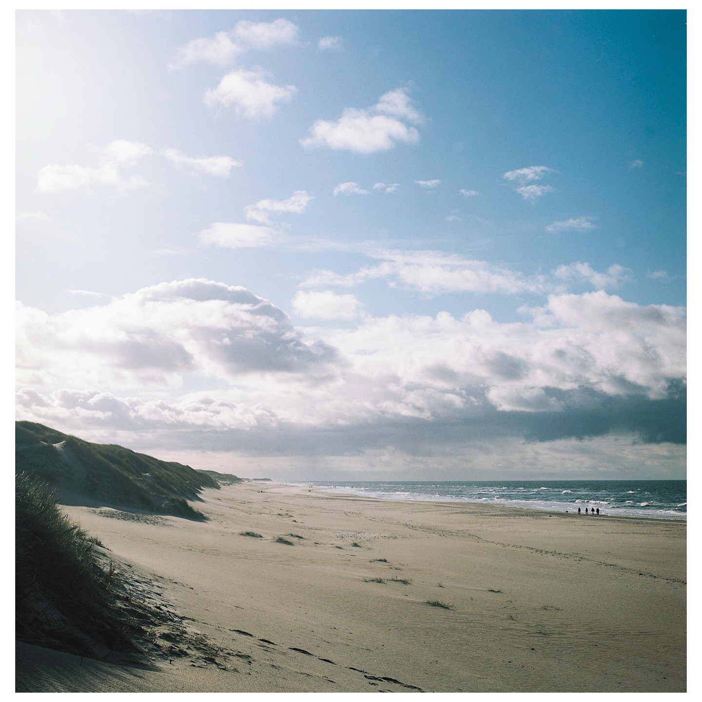A wide sandy beach with dunes on the left and the ocean on the right, under a partly cloudy sky.