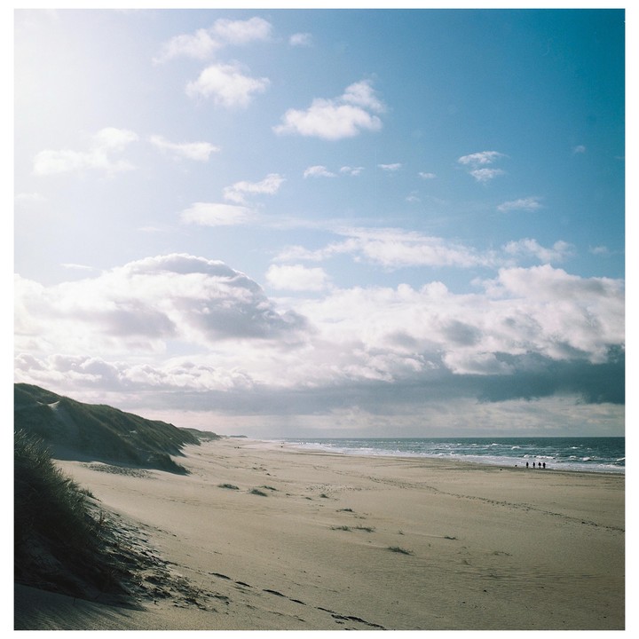 A wide sandy beach with dunes on the left and the ocean on the right, under a partly cloudy sky.
