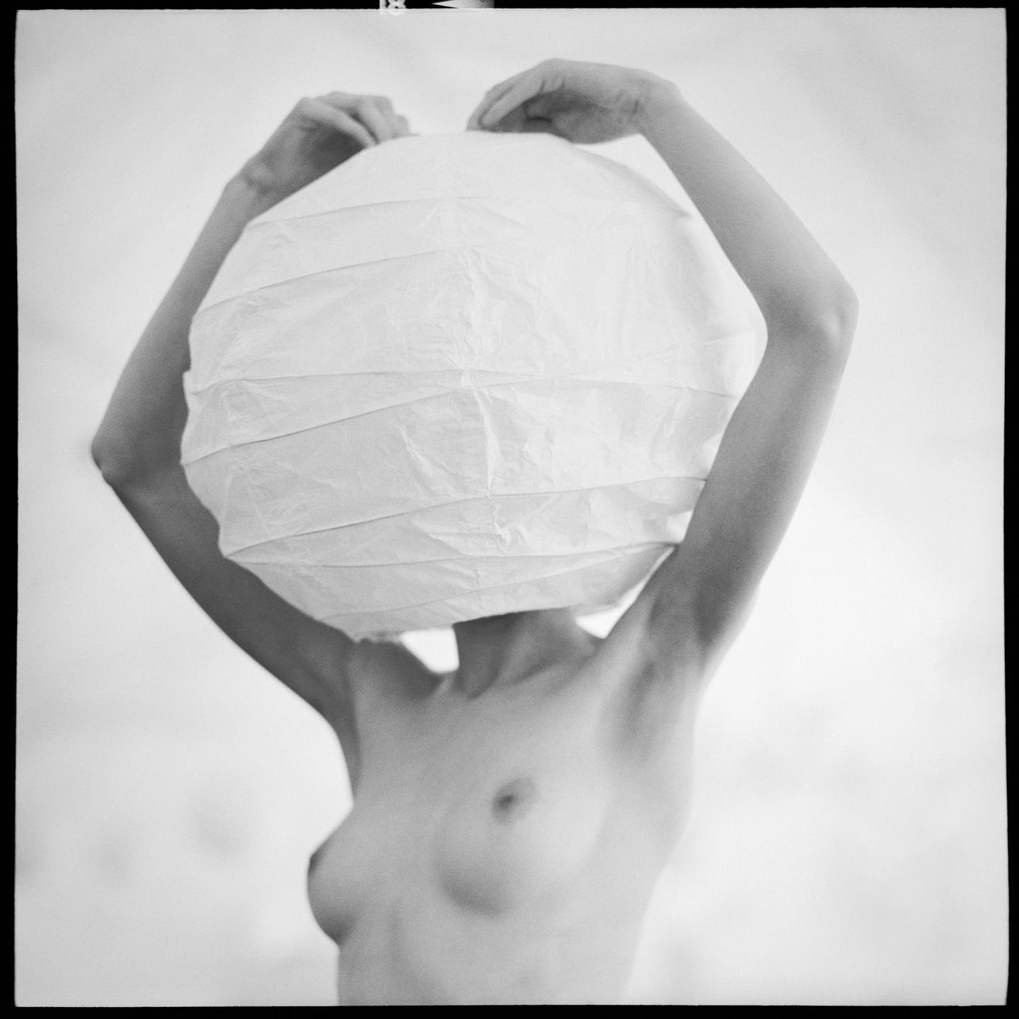 A woman holds a paper lantern over her head, obscuring her face.