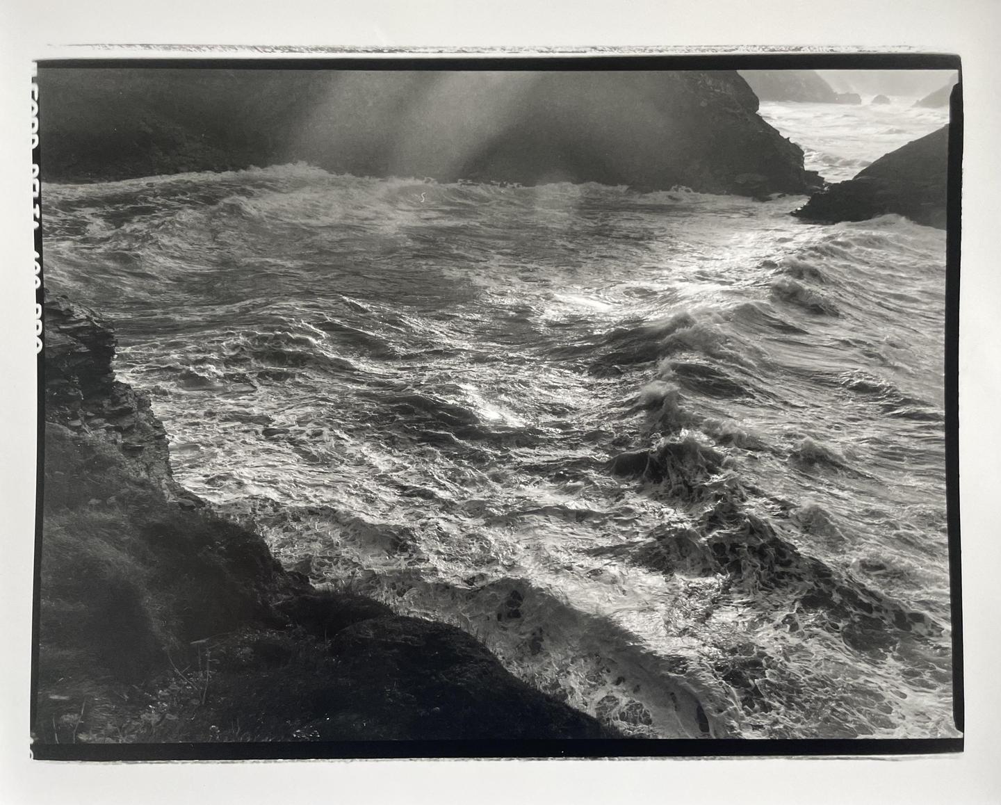 Waves crash against a rocky coastline under a dramatic sky.