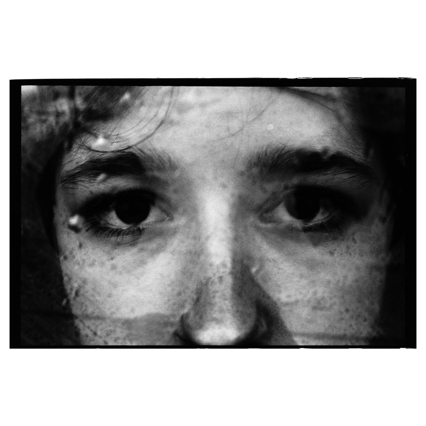 A close-up, black and white portrait shows a person's face with water droplets and streaks.