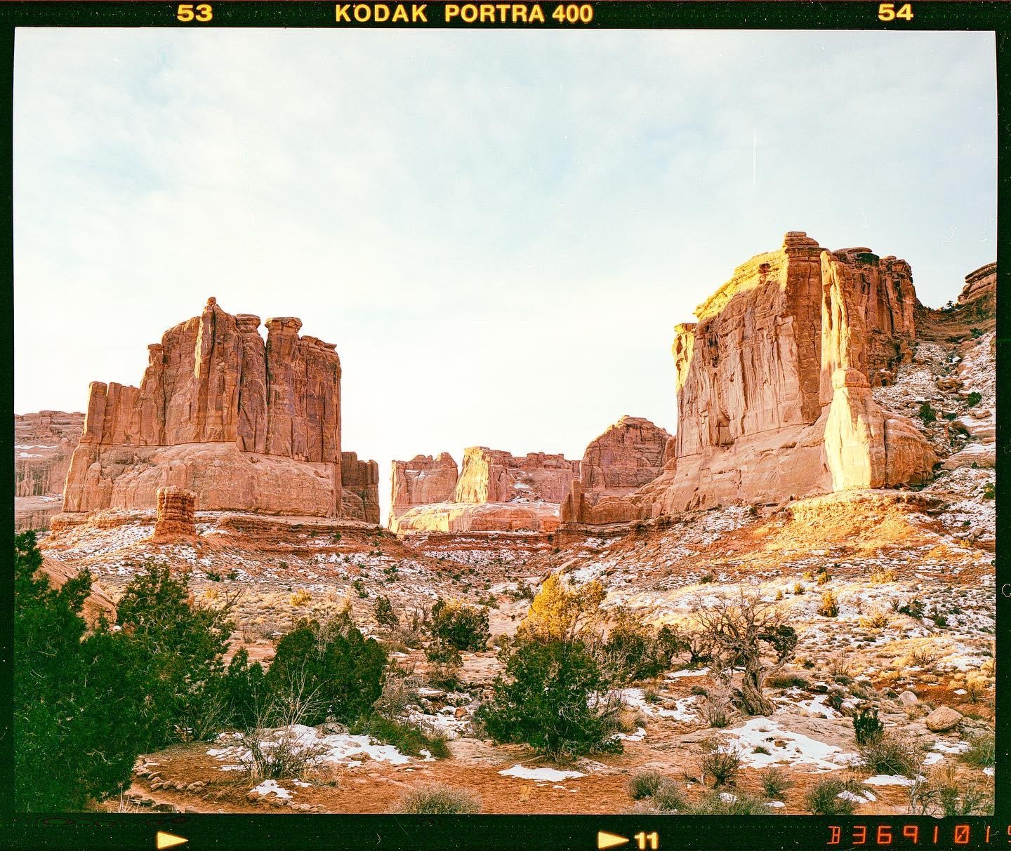 A wide shot shows the red rock formations of Arches National Park with patches of snow on the ground.