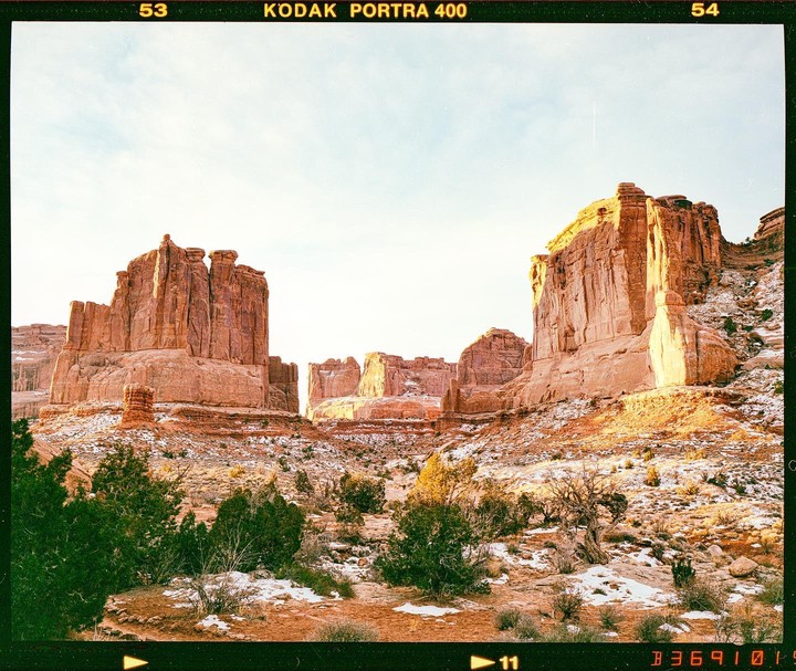 A wide shot shows the red rock formations of Arches National Park with patches of snow on the ground.