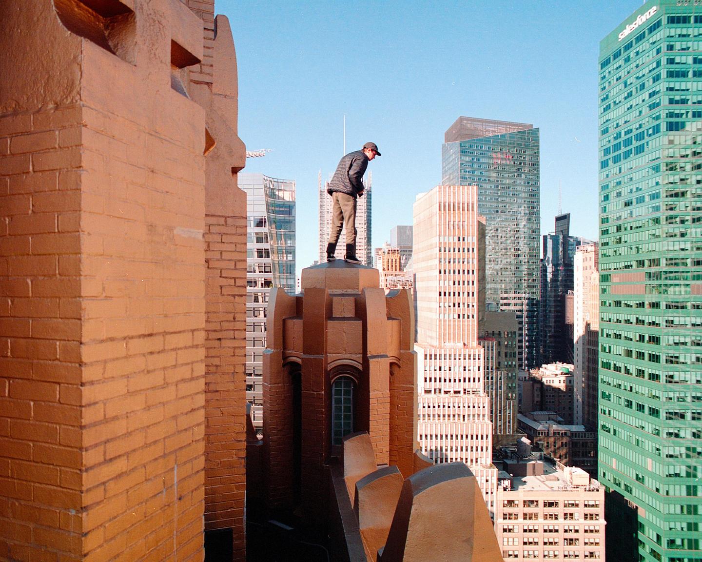 A man stands on a building ledge overlooking a city.