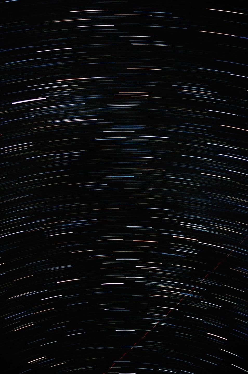 A long exposure photograph captures the movement of stars and satellites across a dark night sky.