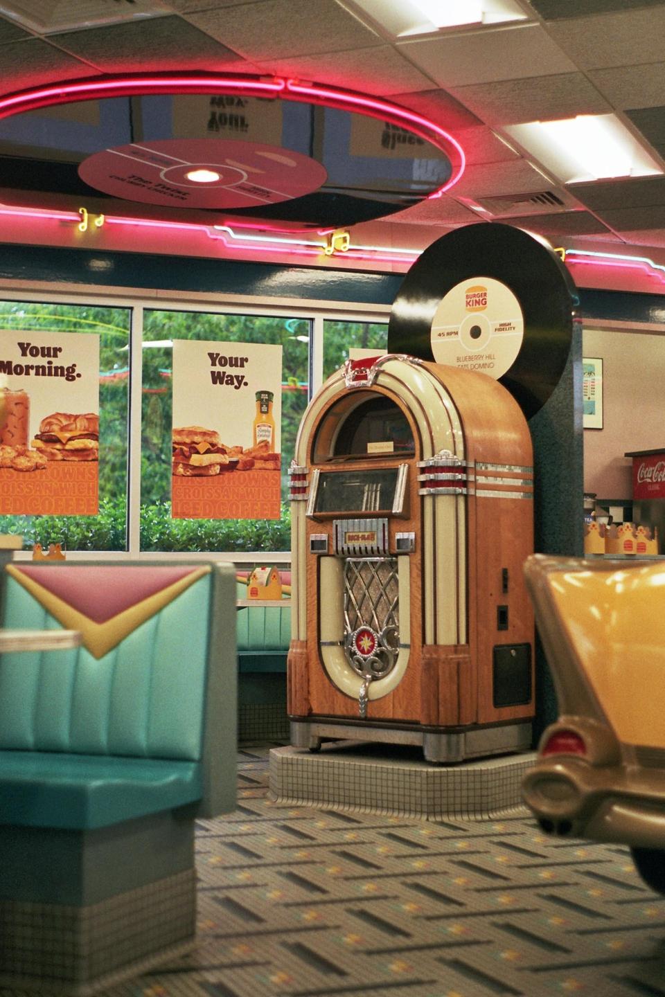 A vintage jukebox stands in a Burger King restaurant with neon lights and booths.