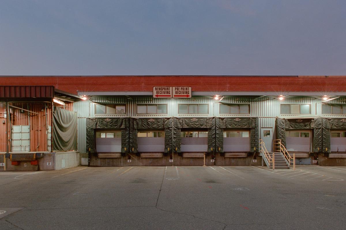 A long exterior shot of a loading dock with multiple bays and an empty asphalt lot in front.