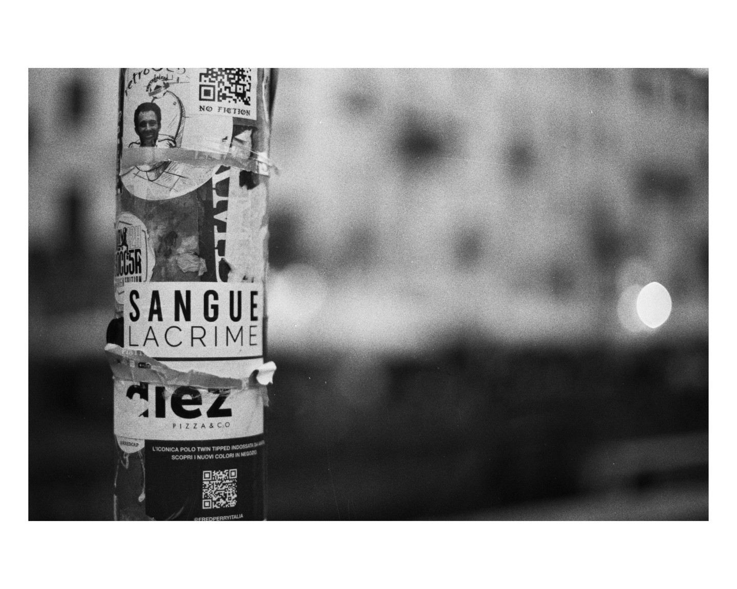 A pole covered in torn posters and advertisements stands on a street with a blurred background.