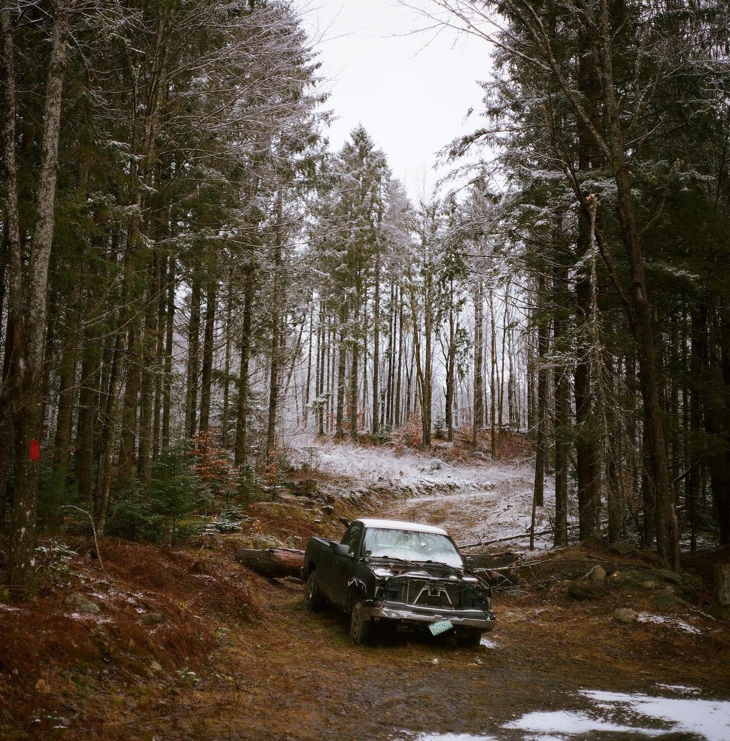 A broken-down truck sits on a muddy road in a snowy forest.