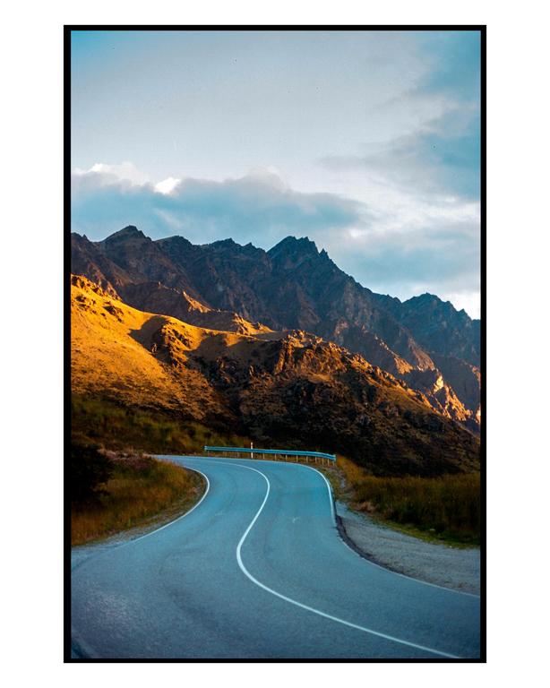 A winding road leads through a mountainous landscape with golden light on the peaks.