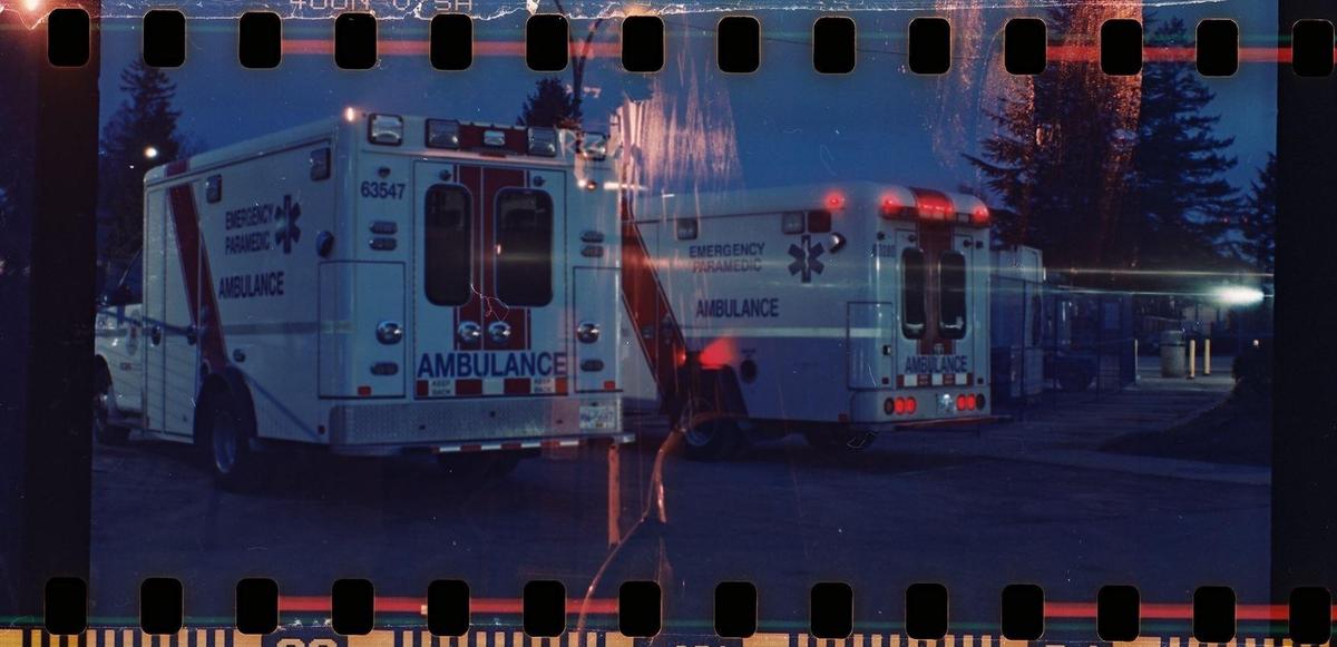 Two ambulances are parked at night with their lights on, and the image has light leaks and film borders.