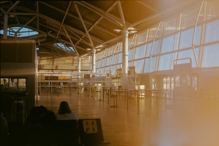 A woman sits in an airport terminal with large windows and a high ceiling.