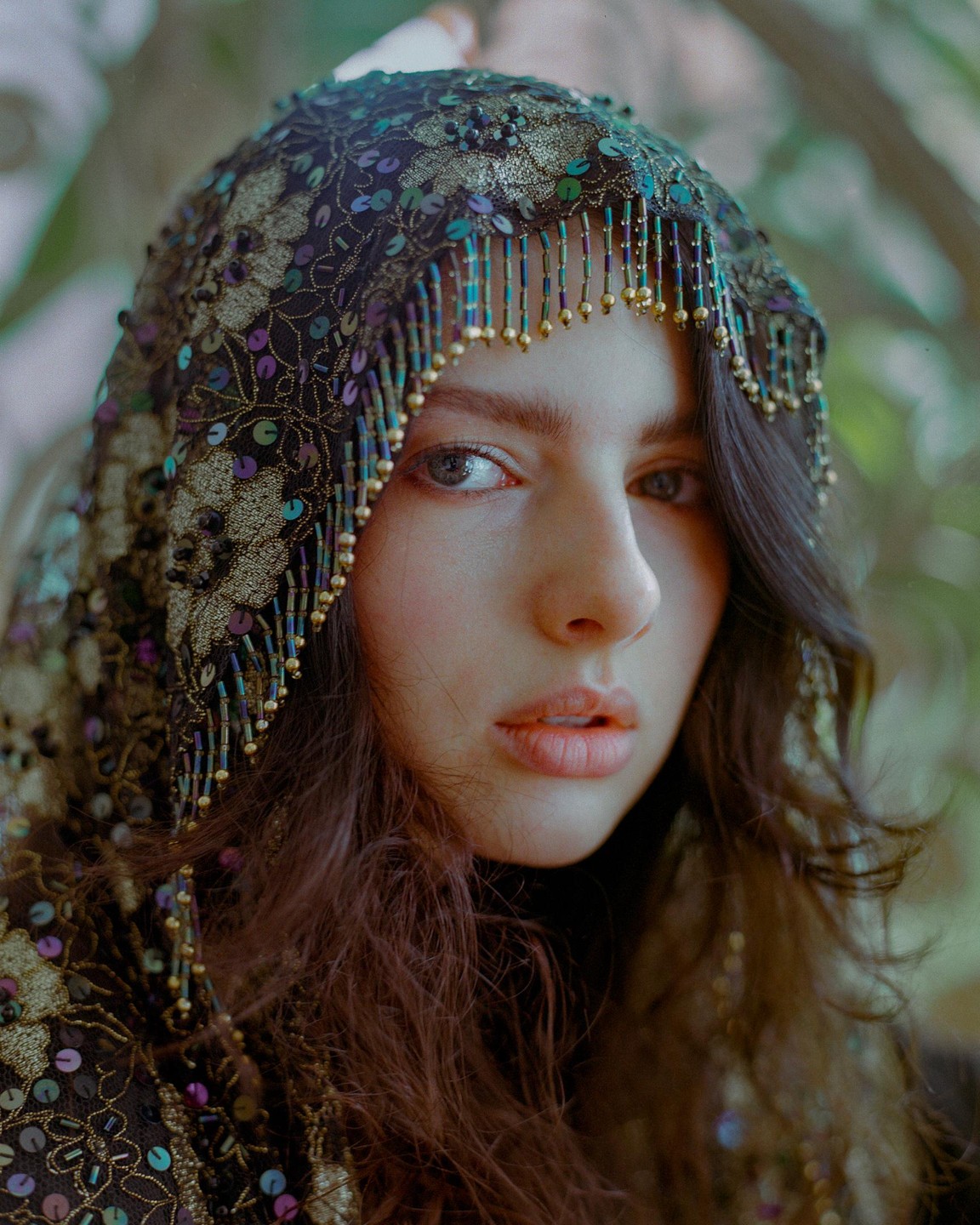 A woman with long, dark hair wears an ornate, beaded hood with sequins.