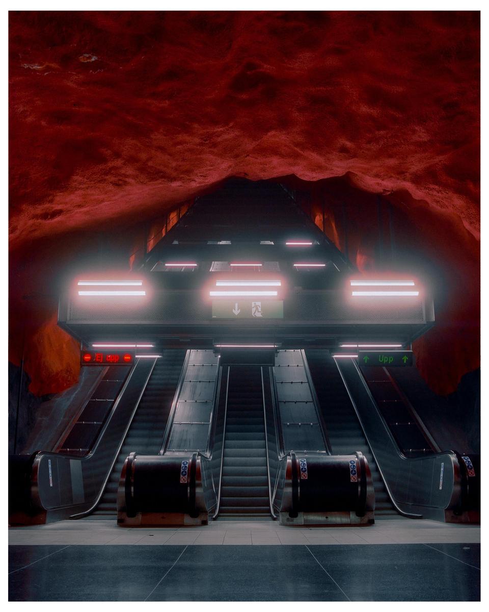 Three escalators lead up to a red, cavernous ceiling in a subway station.