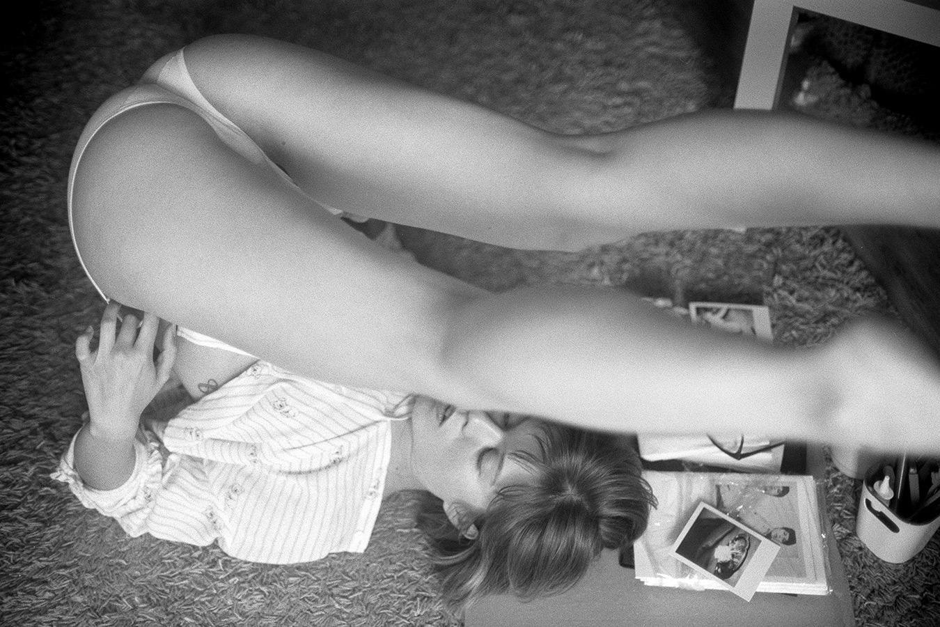 A woman lies on her back on a carpet with her legs raised and bent over her head.