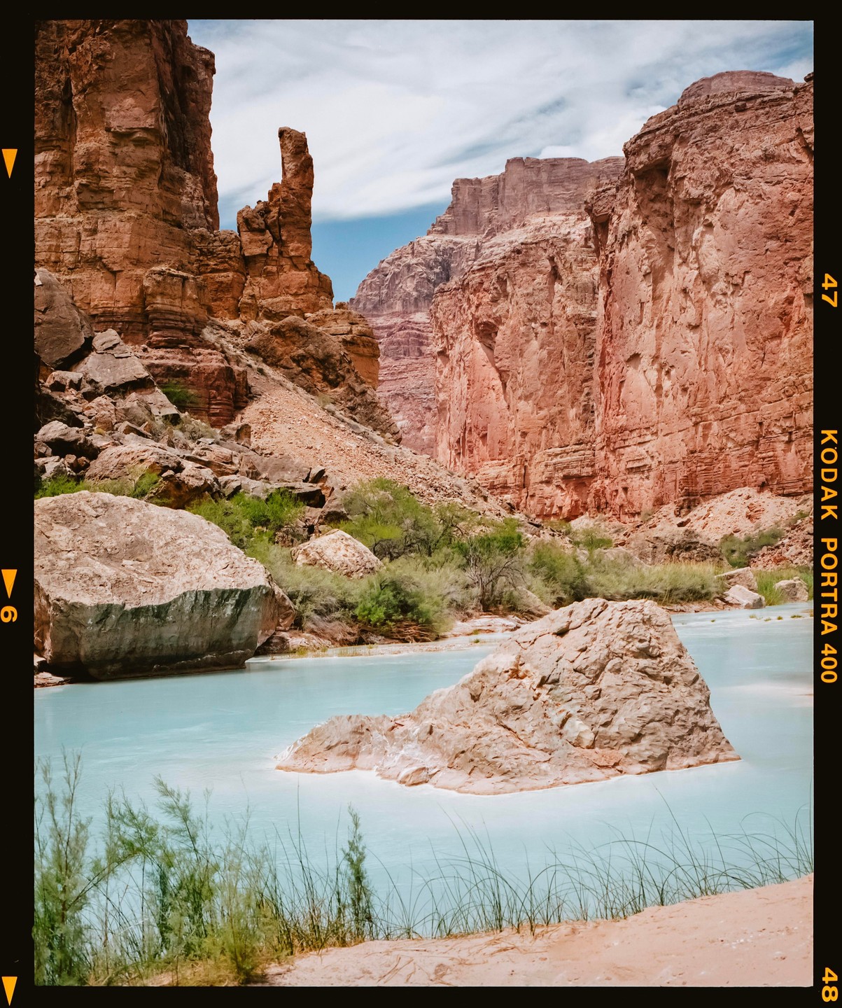 A light blue river flows through a canyon with tall red rock formations and green vegetation.