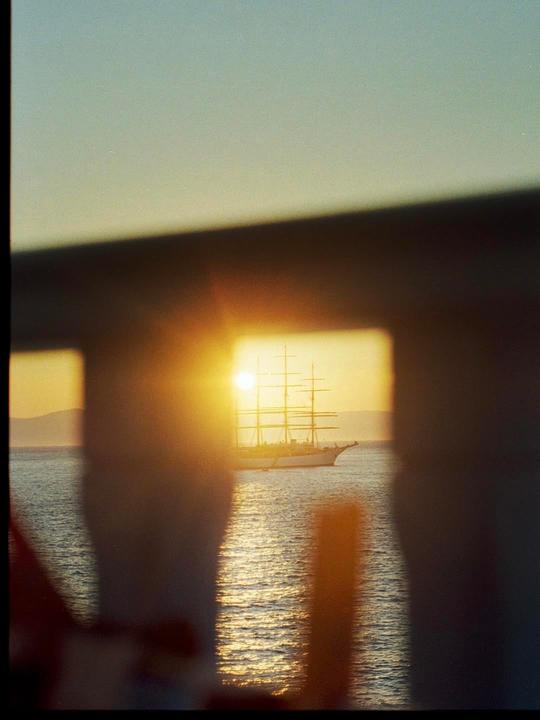 A sailboat is visible on the water through a railing at sunset.