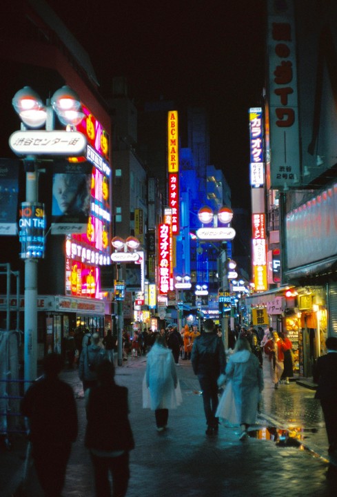A street in Tokyo is filled with people and neon signs at night.