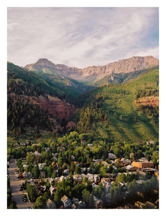 A town with many trees and houses sits at the base of a large mountain range.