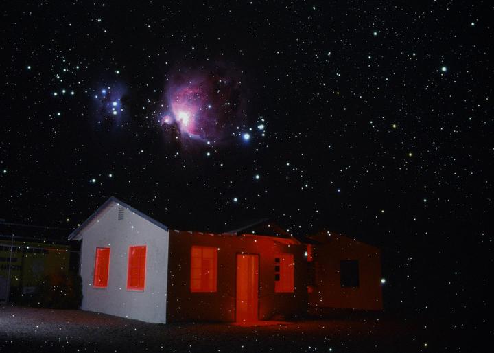 A double exposure shows an abandoned house with red light emanating from its windows and door, set against a night sky filled with stars and the Orion Nebula.