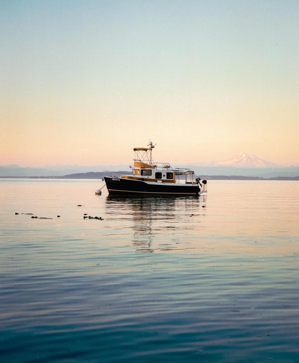 A boat floats on calm water with a mountain in the distance under a pastel sky.