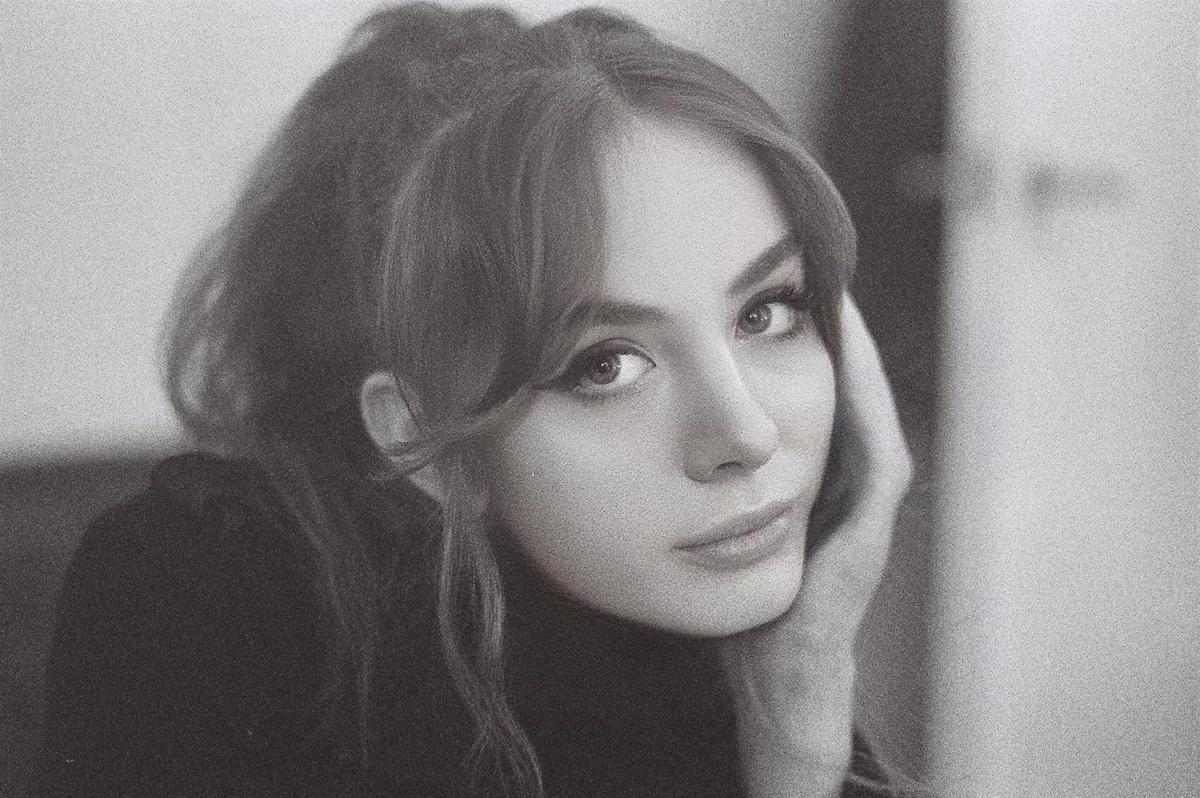 A woman with bangs and long hair looks at the viewer, resting her head on her hand.