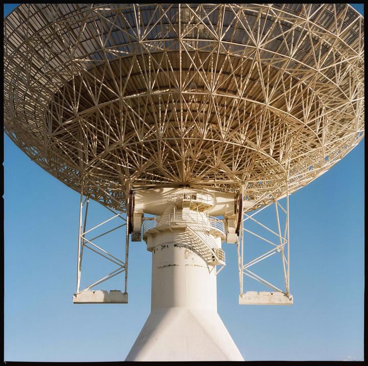 A large white satellite dish is shown from below against a clear blue sky.