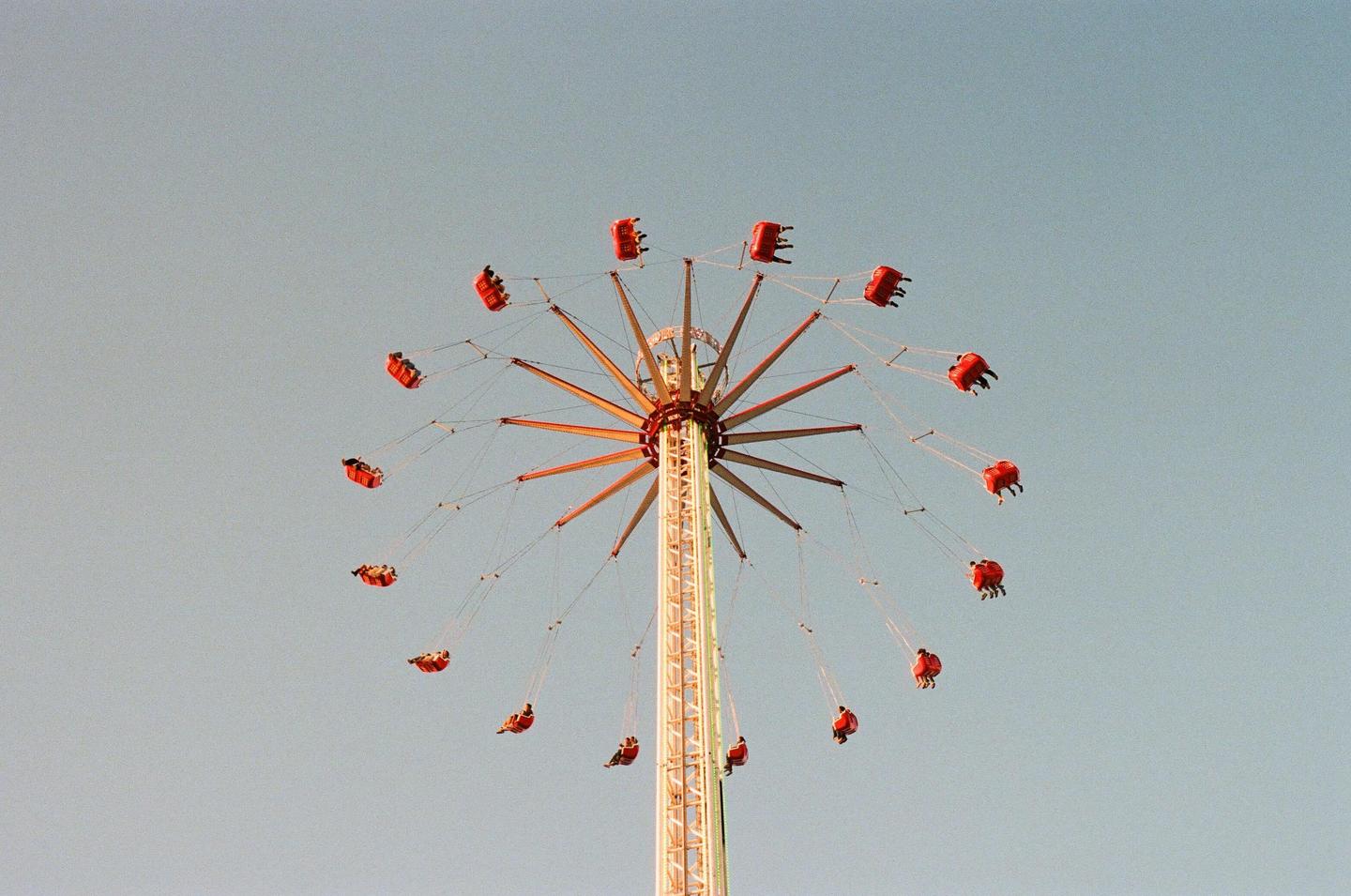 A swing ride with people in red seats is captured against a clear sky.