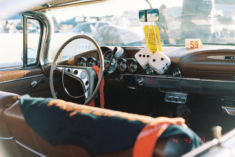 A pair of fuzzy dice hangs from the rearview mirror of a vintage car.