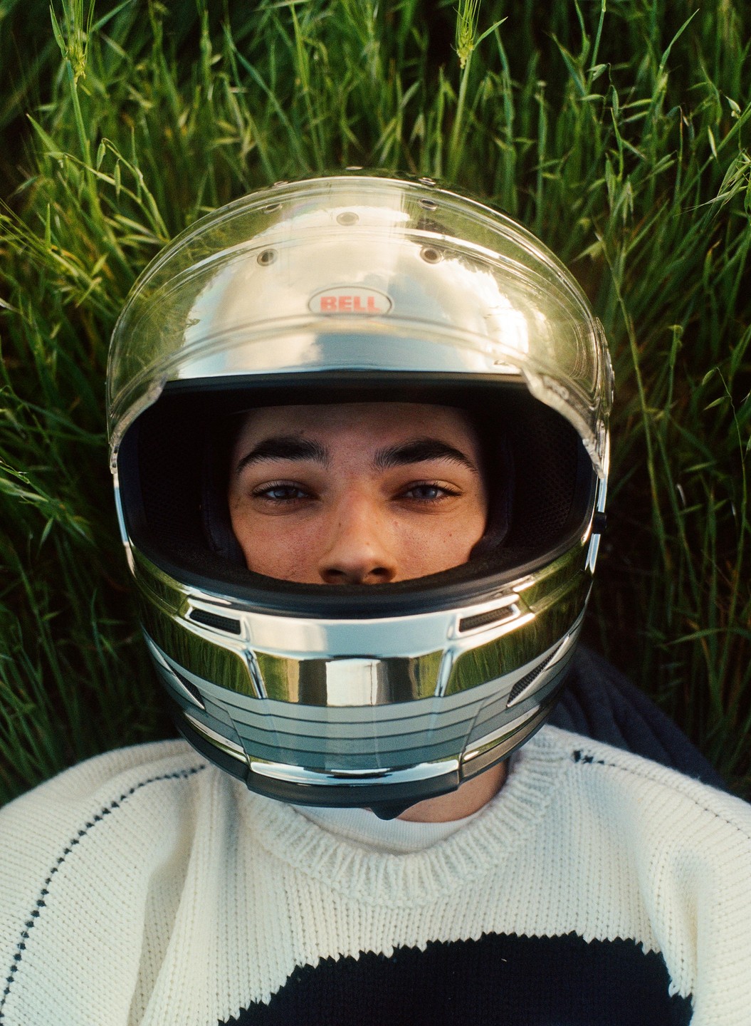 A man wearing a motorcycle helmet is lying in tall green grass.