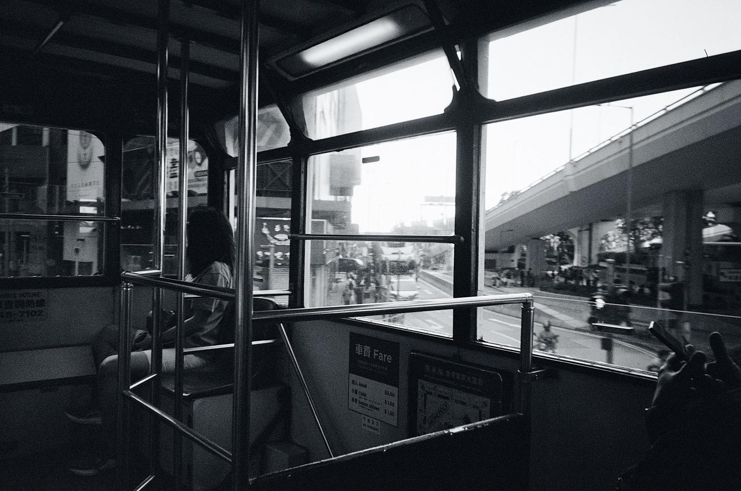 A woman sits inside a tram looking out the window at a street with an overpass.