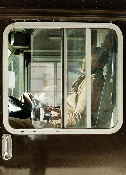 A man sits in the driver's seat of a vehicle, seen through a window.