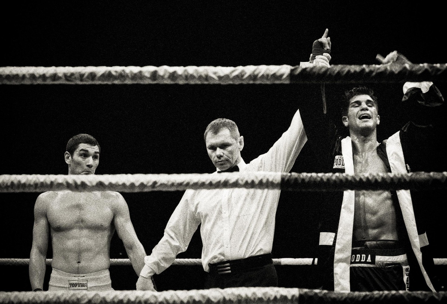 A referee raises the arm of a victorious boxer while the other boxer looks on in a boxing ring.