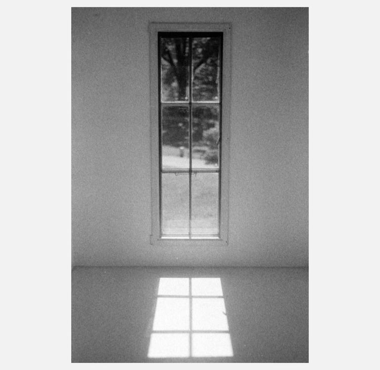 A tall, narrow window with multiple panes is centered on a white wall, casting a grid of light onto the floor.
