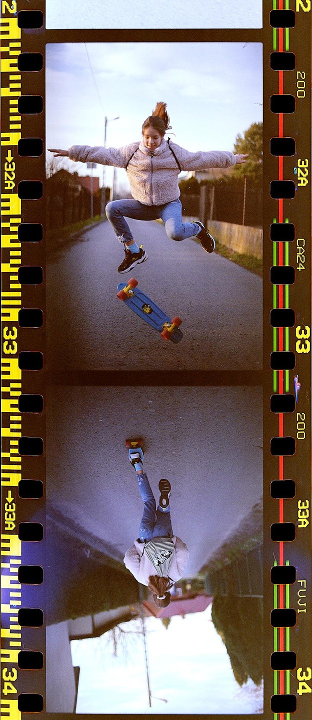 A girl jumps in the air with a skateboard below her, with an inverted reflection of the scene below.