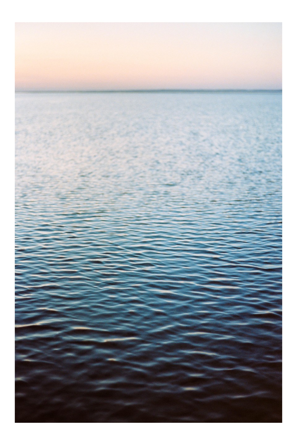 The ocean stretches to the horizon under a pastel sky at sunset.
