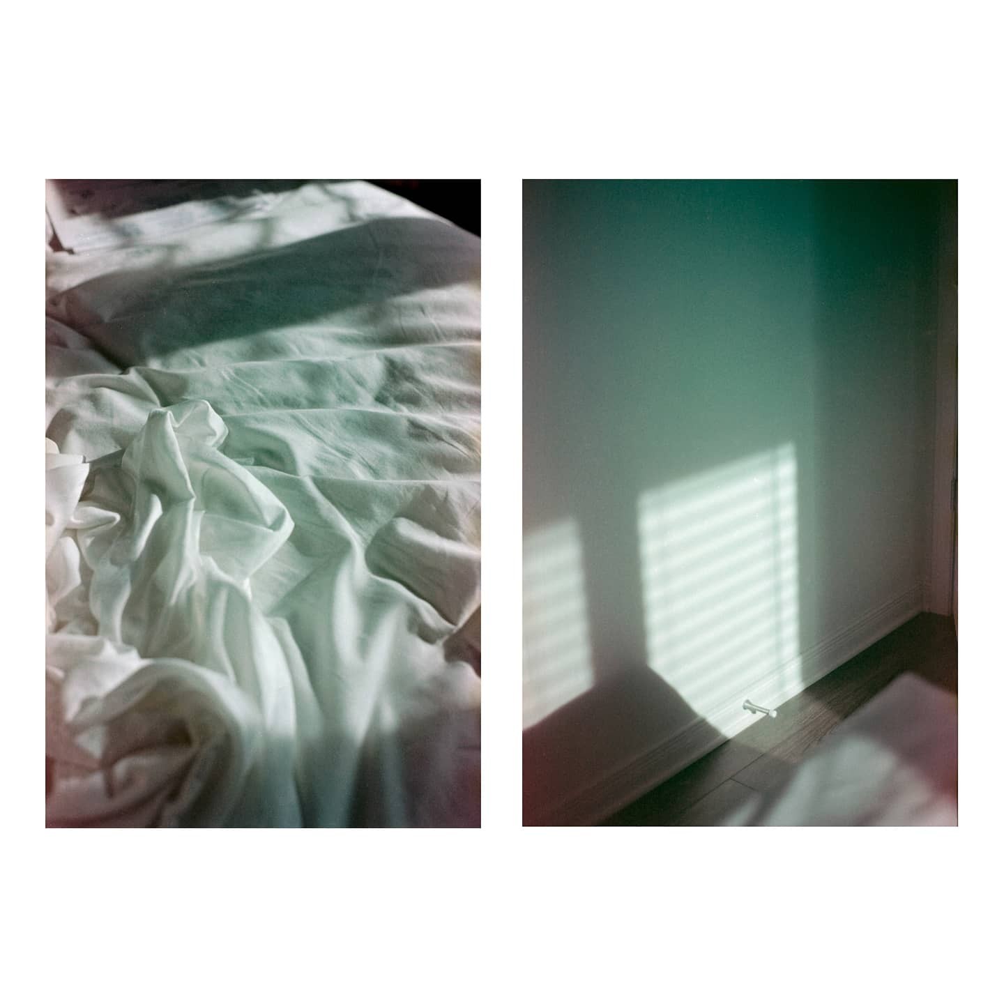 Sunlight casts shadows on a rumpled bed and a wall with a baseboard.