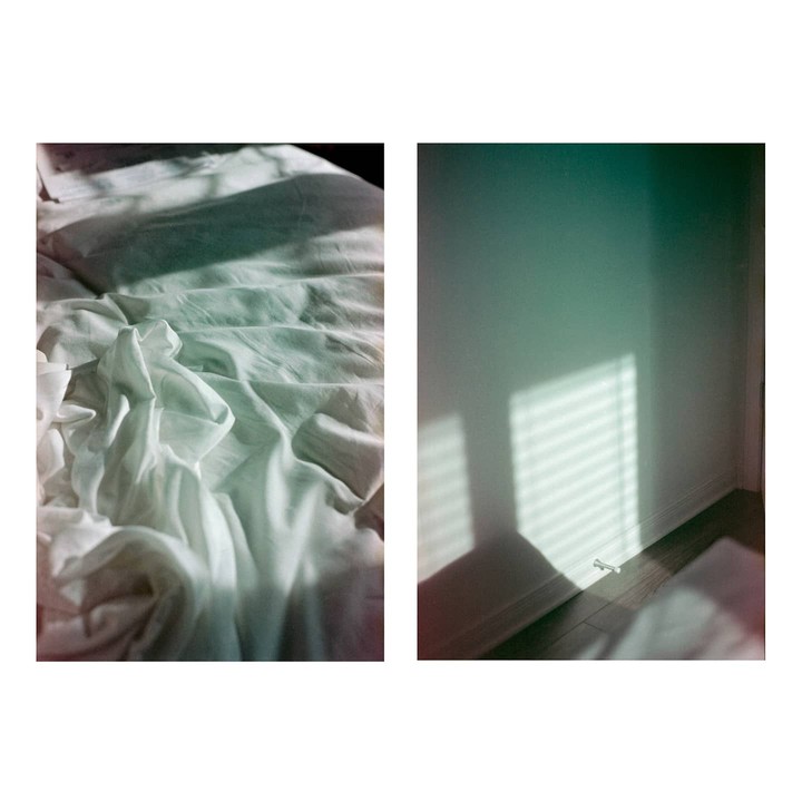 Sunlight casts shadows on a rumpled bed and a wall with a baseboard.