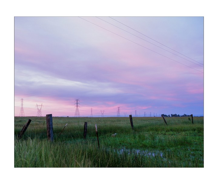 A field with power lines and transmission towers is visible under a colorful sky.