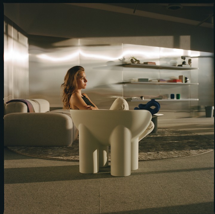 A woman sits in a modern white chair in a room with metallic walls and shelves.