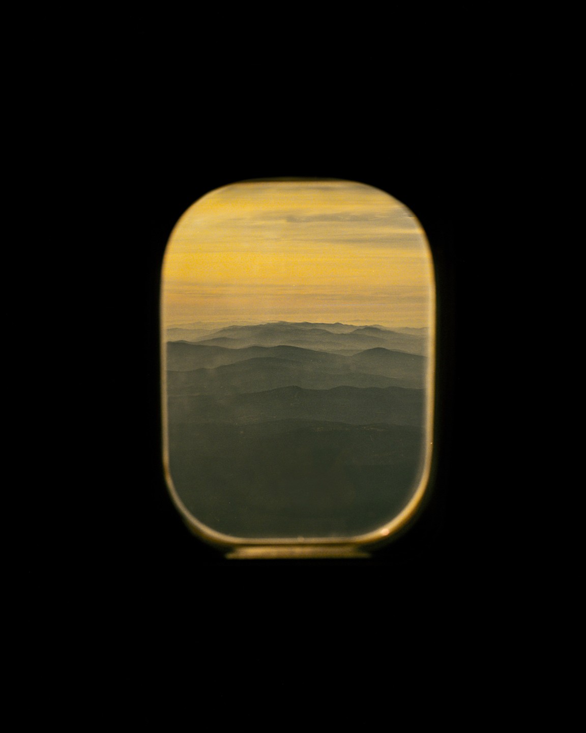A view of hazy mountains and a golden sky is visible through an airplane window.